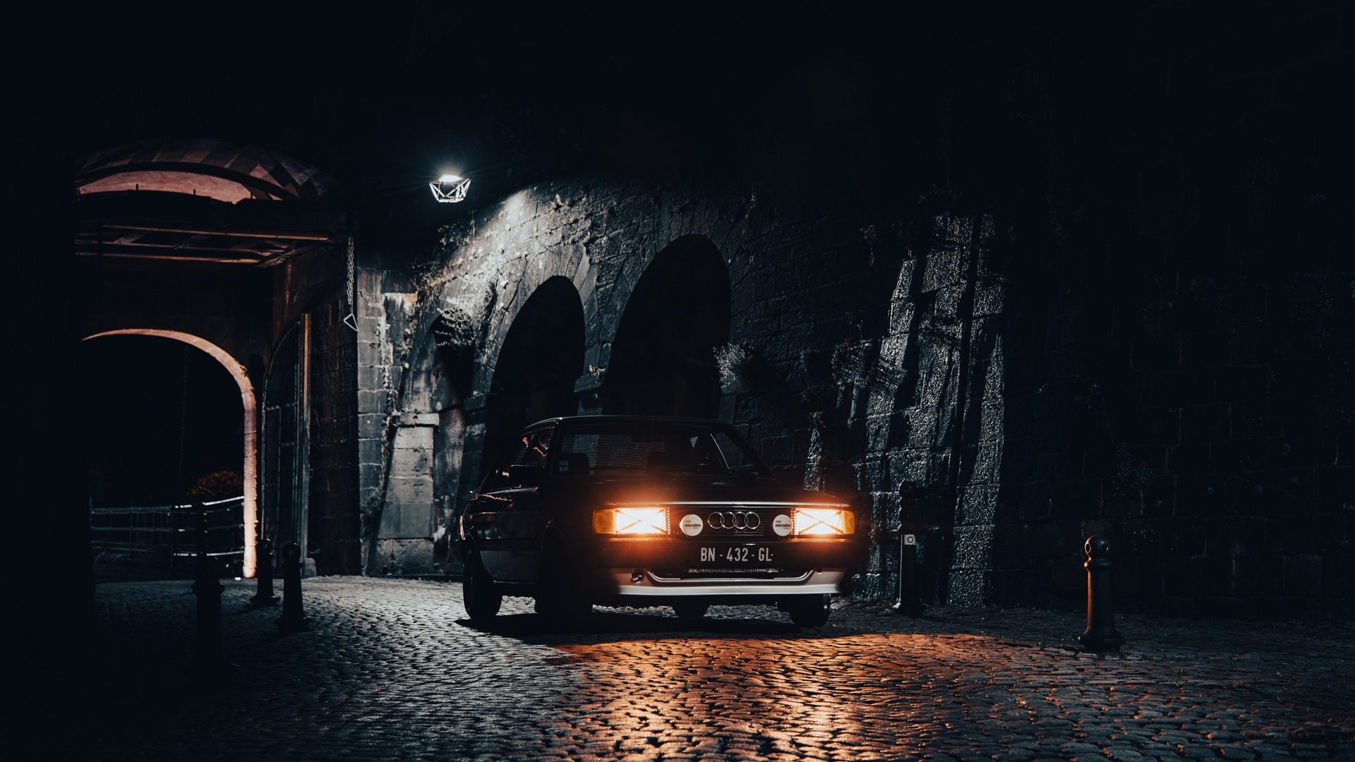 Audi A80 ancienne sous une arche historique Voiture Audi A80 circulant de nuit sous une arche historique éclairée