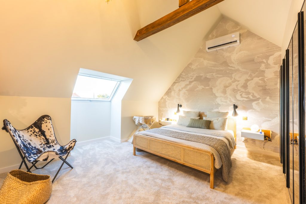 Photographe immobilier : chambre mansardée scandinave, lit rotin, fauteuil papillon, décoration moderne et lumineuse.