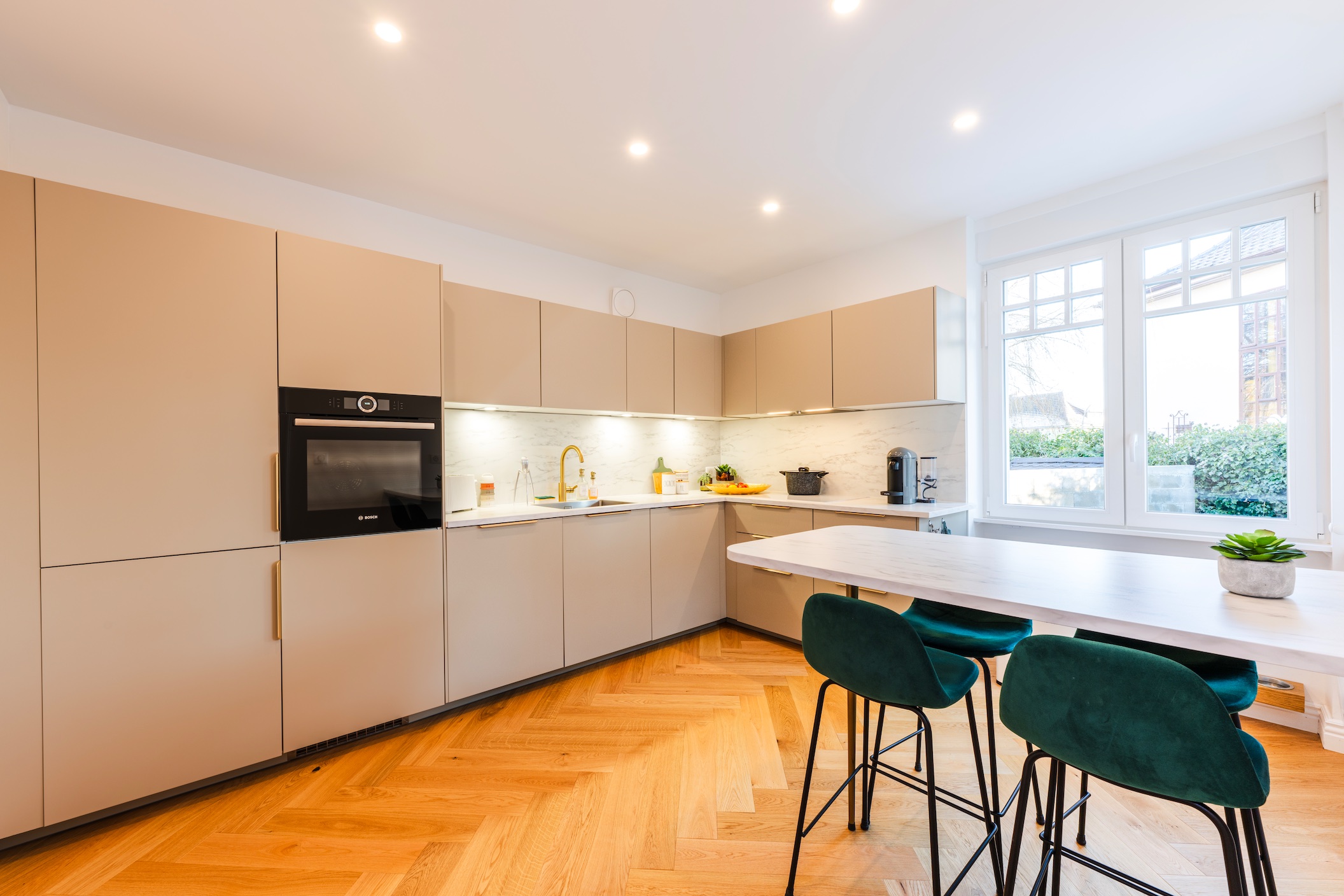 cuisine-moderne-scandinave-ilot-taupe-parquet-chevron-immobilier Cuisine scandinave moderne et lumineuse. Mobilier taupe minimaliste, parquet chevron, îlot blanc et tabourets verts.