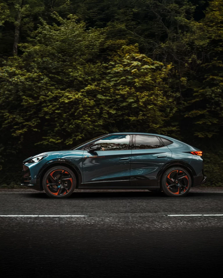 Photographie dynamique d'un Cupra Tavascan bleu, profil en mouvement sur la route des vins d'Alsace.