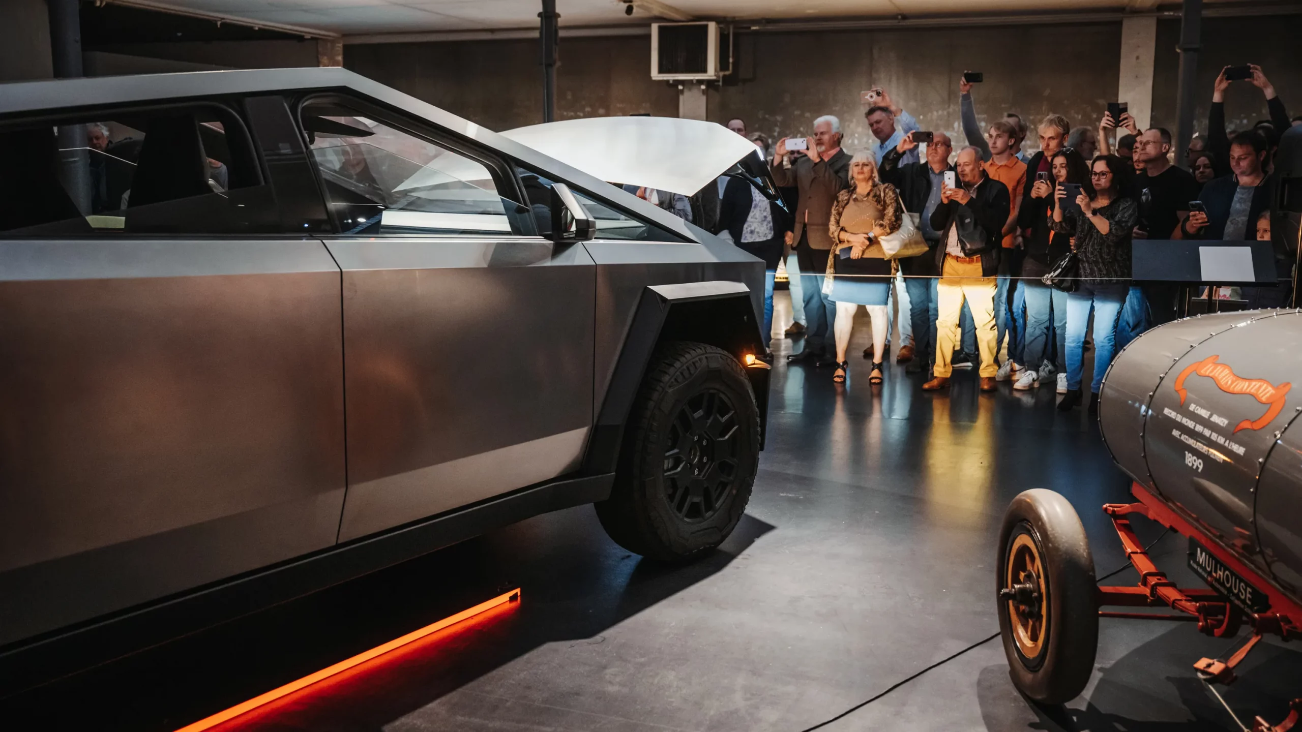 cybertruck-musee-mulhouse-foule-innovation-heritage Cybertruck Tesla exposé à Mulhouse devant une foule, en contraste avec une voiture historique 1899.