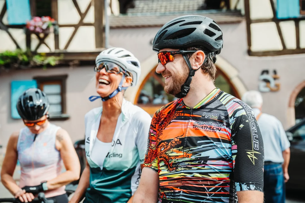 Cyclistes souriants lors des Boucles Škoda à Colmar devant des maisons à colombages alsaciennes.