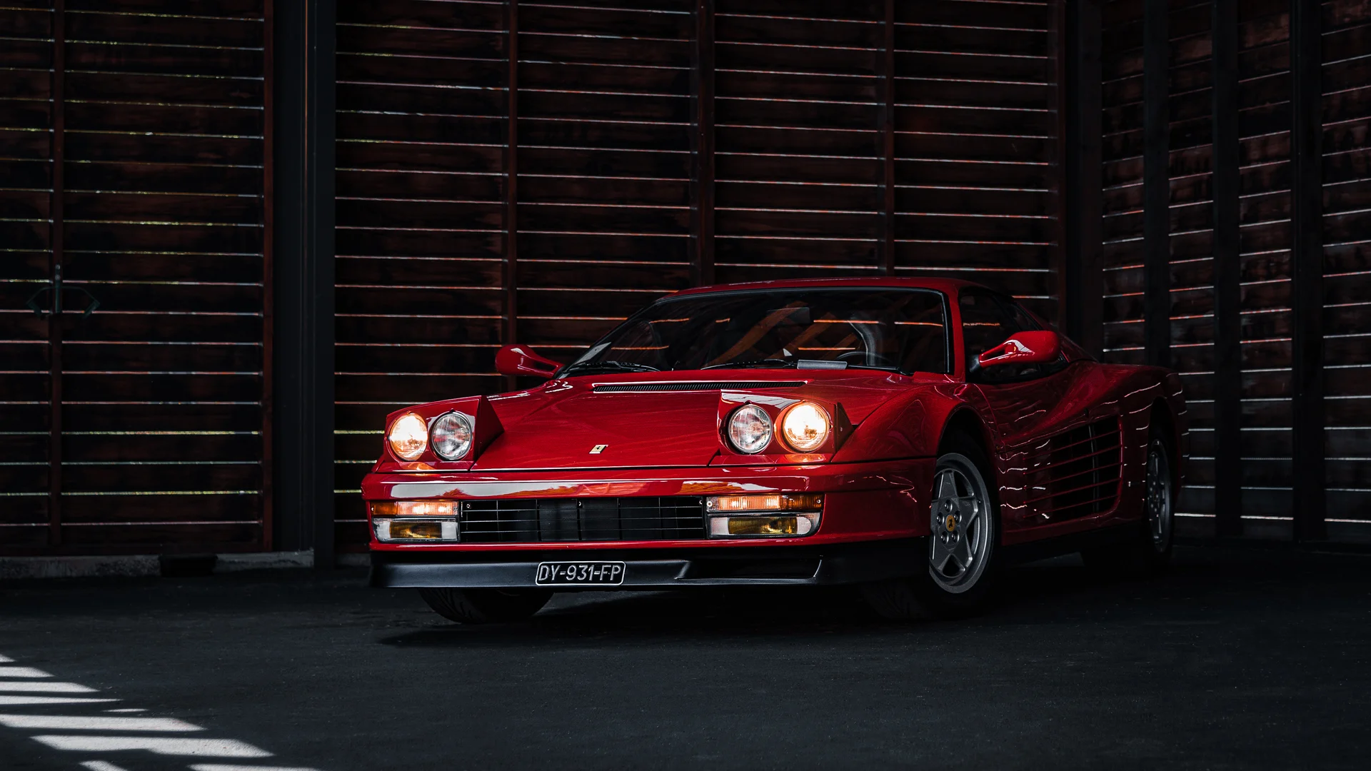 ferrari-testarossa-rouge-phares-ouverts-garage-sombre Ferrari Testarossa rouge classique, phares ouverts, photo statique studio, patrimoine automobile collection.