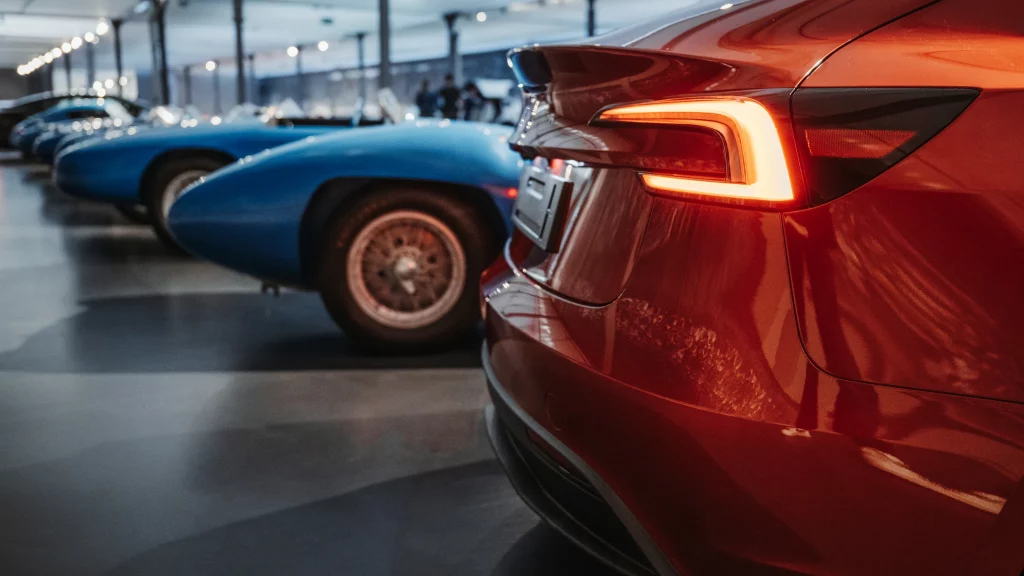 Gros plan sur le feu arrière rouge d'une Tesla contrastant avec des voitures de sport bleues classiques à Mulhouse.